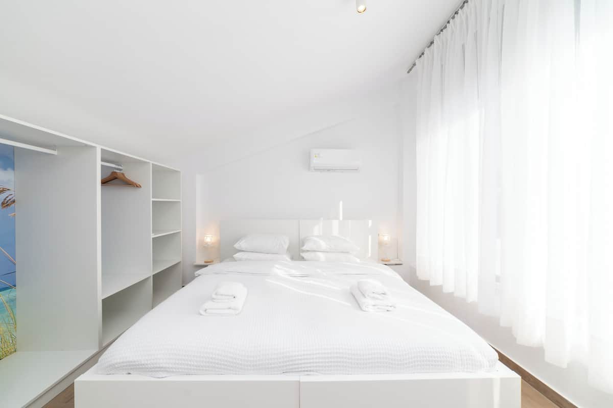 A modern bedroom with a large bed, white walls, and a built-in wardrobe.
