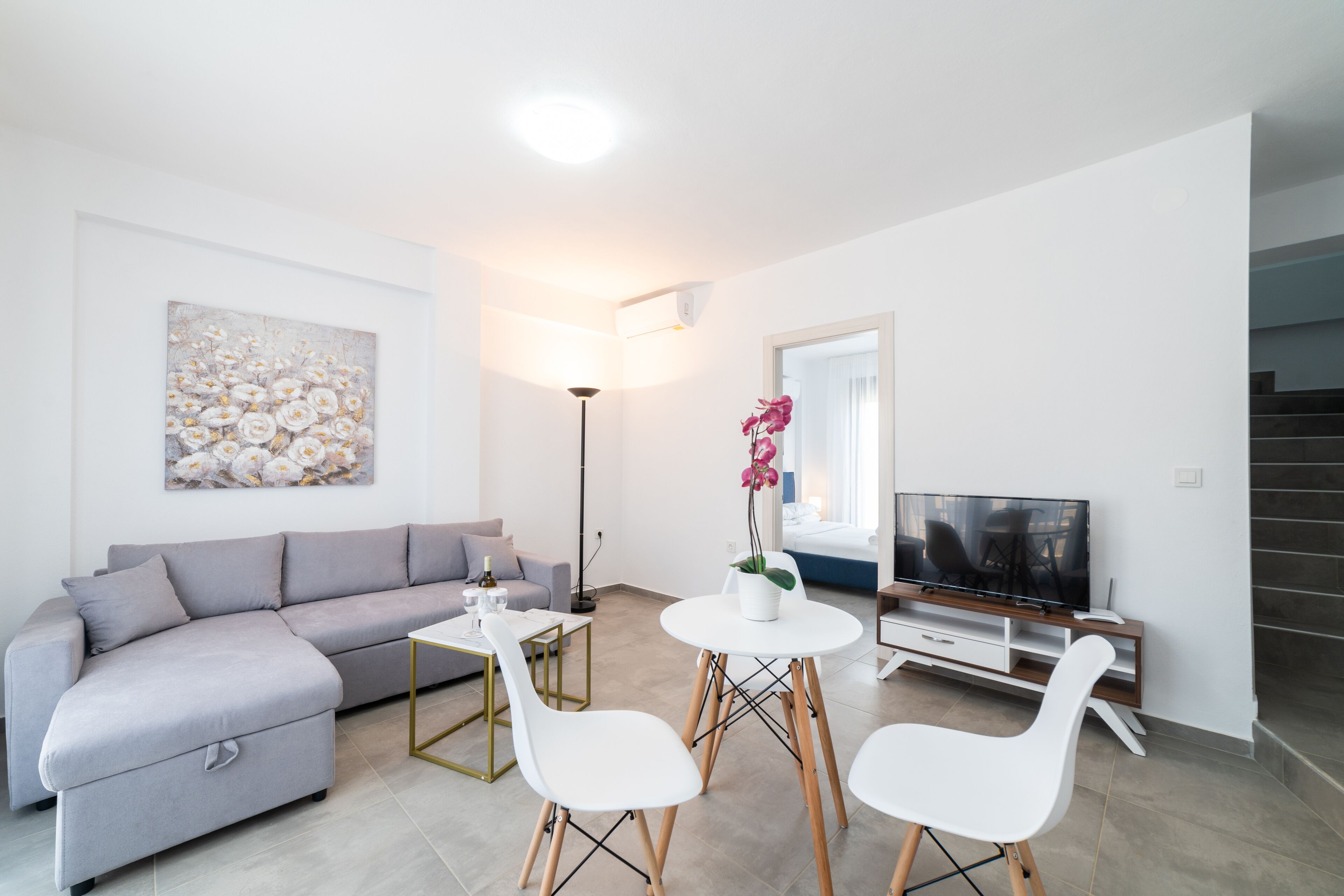 A modern living room with a grey sofa, white chairs, a coffee table, a TV, and a painting on the wall.