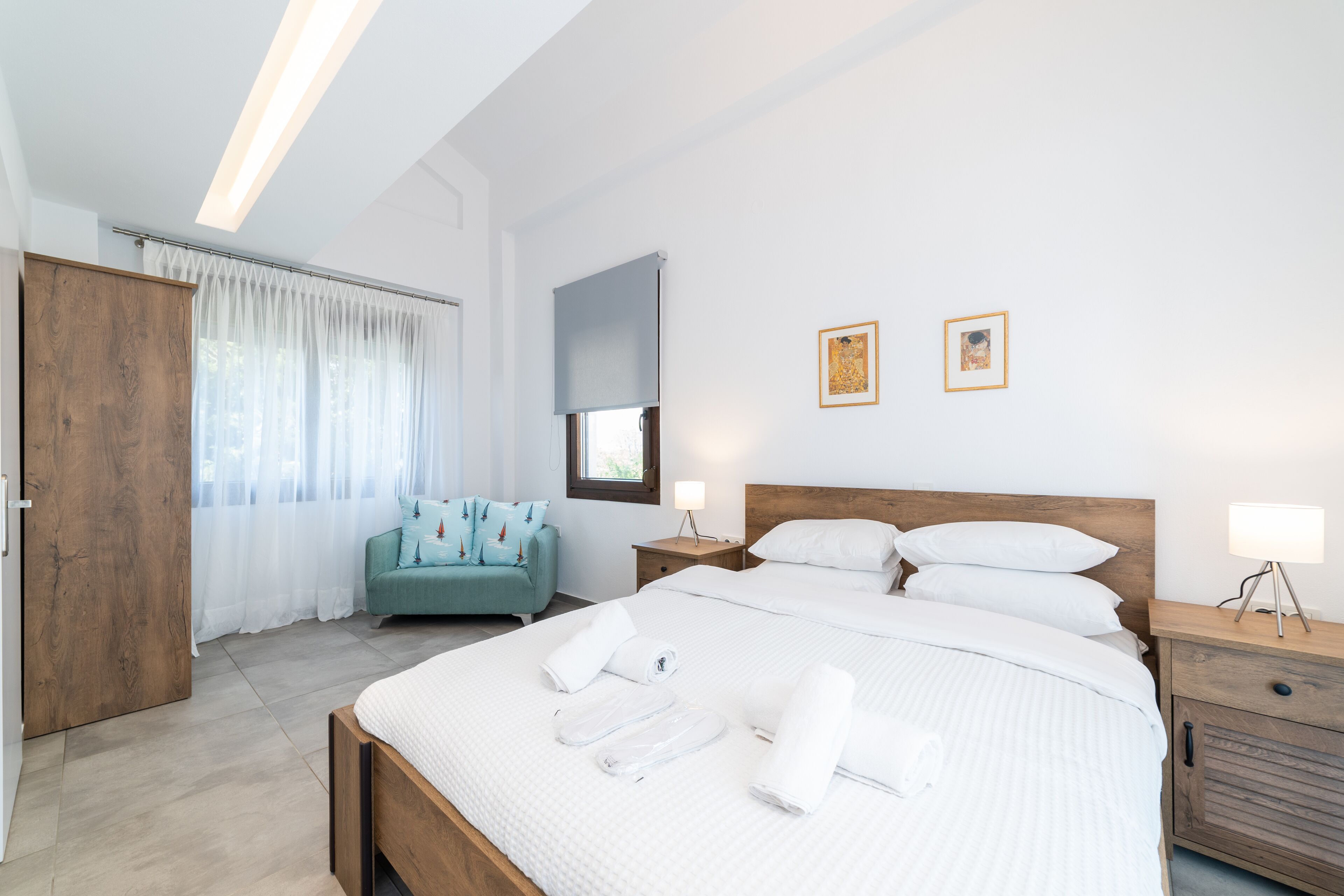 Un dormitorio moderno con una cama grande, un armario de madera, un sofá color turquesa y dos mesitas de noche con lámparas.