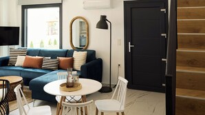 Una sala de estar moderna con un sofá azul, sillas blancas, una mesa redonda y una puerta negra.