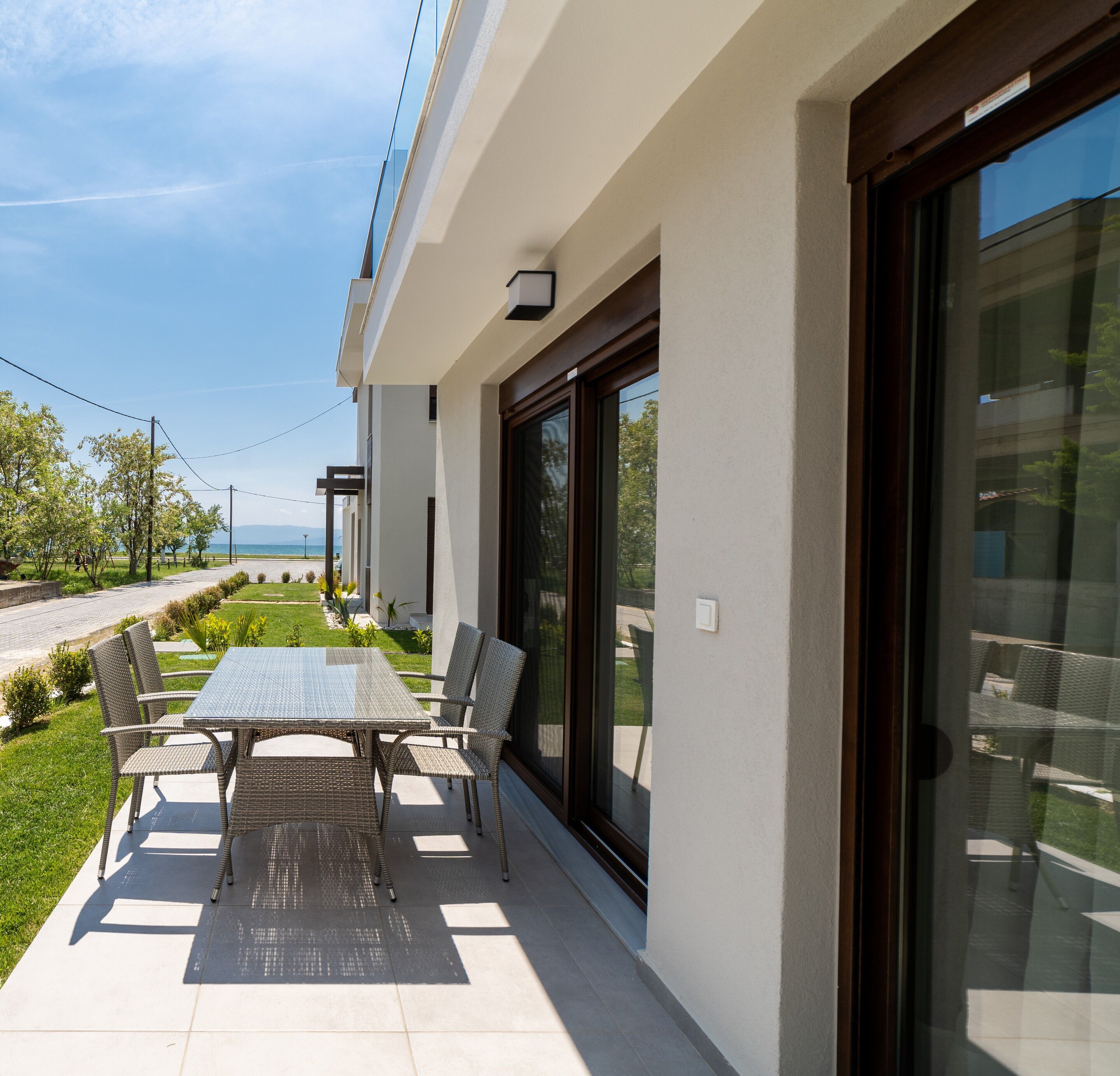 Un patio exterior moderno con una mesa, sillas, un ventanal de vidrio y vistas al mar.