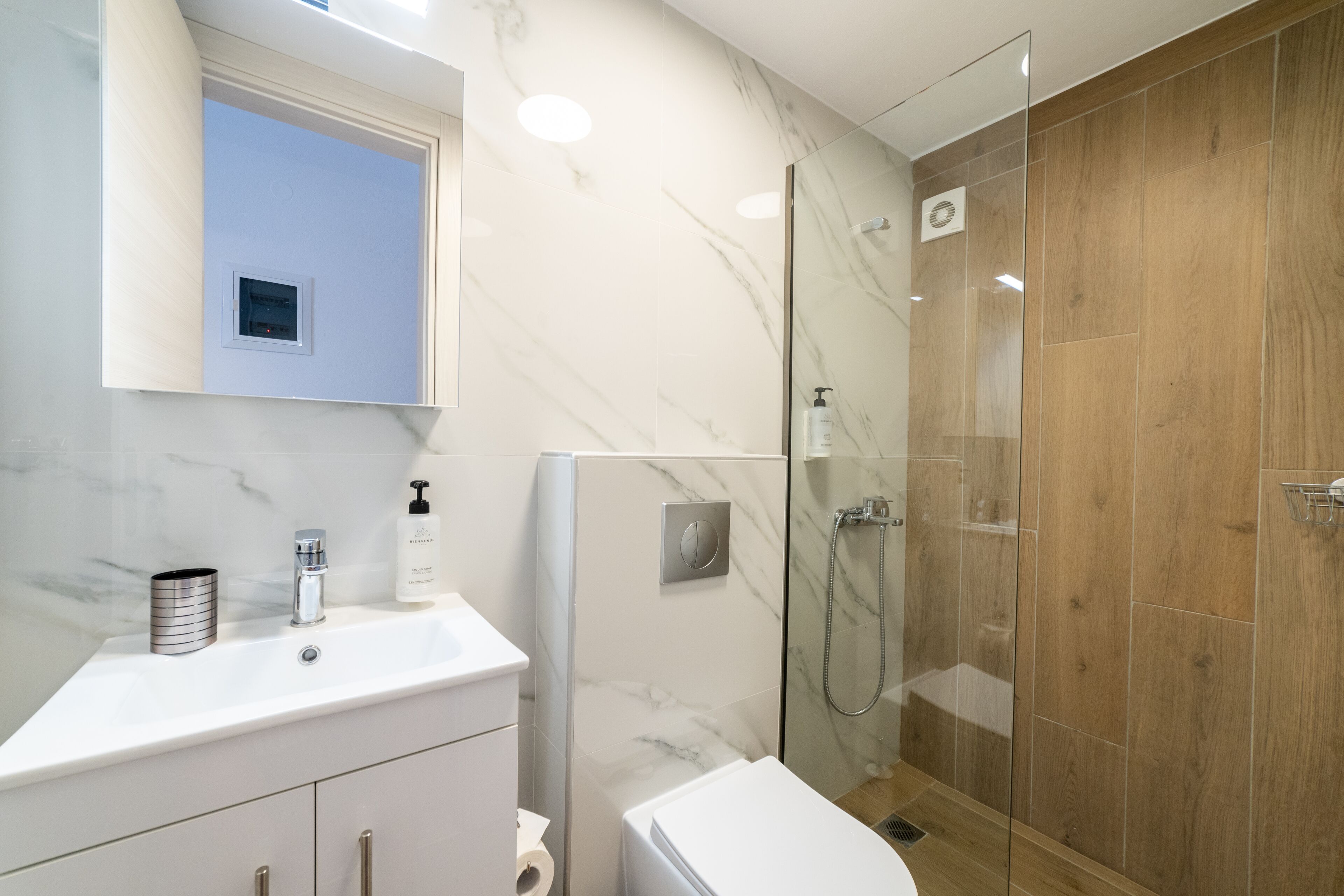 A modern bathroom with a marble sink, a toilet, and a glass-enclosed shower.