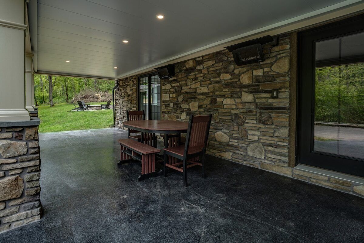 An outdoor patio with a stone wall, a wooden table, and chairs.