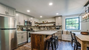 A modern kitchen with a central island, stainless steel appliances, and a stone backsplash. - Fall Brook: 3 bedroom cabin by waterfalls and hiking trail (Penn Yan)