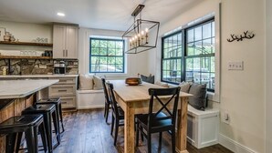 A modern kitchen with a large island, wooden flooring, and a dining area with a bench. - Fall Brook: 3 bedroom cabin by waterfalls and hiking trail (Penn Yan)