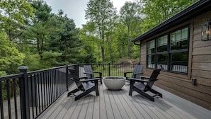 A deck with four chairs and a large planter, surrounded by a wooden deck and a metal railing, overlooking a forested area. - Fall Brook: 3 bedroom cabin by waterfalls and hiking trail (Penn Yan)
