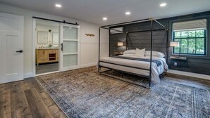 A bedroom with a four-poster bed, a large window, and a view of a wooden cabinet and mirror. - Fall Brook: 3 bedroom cabin by waterfalls and hiking trail (Penn Yan)