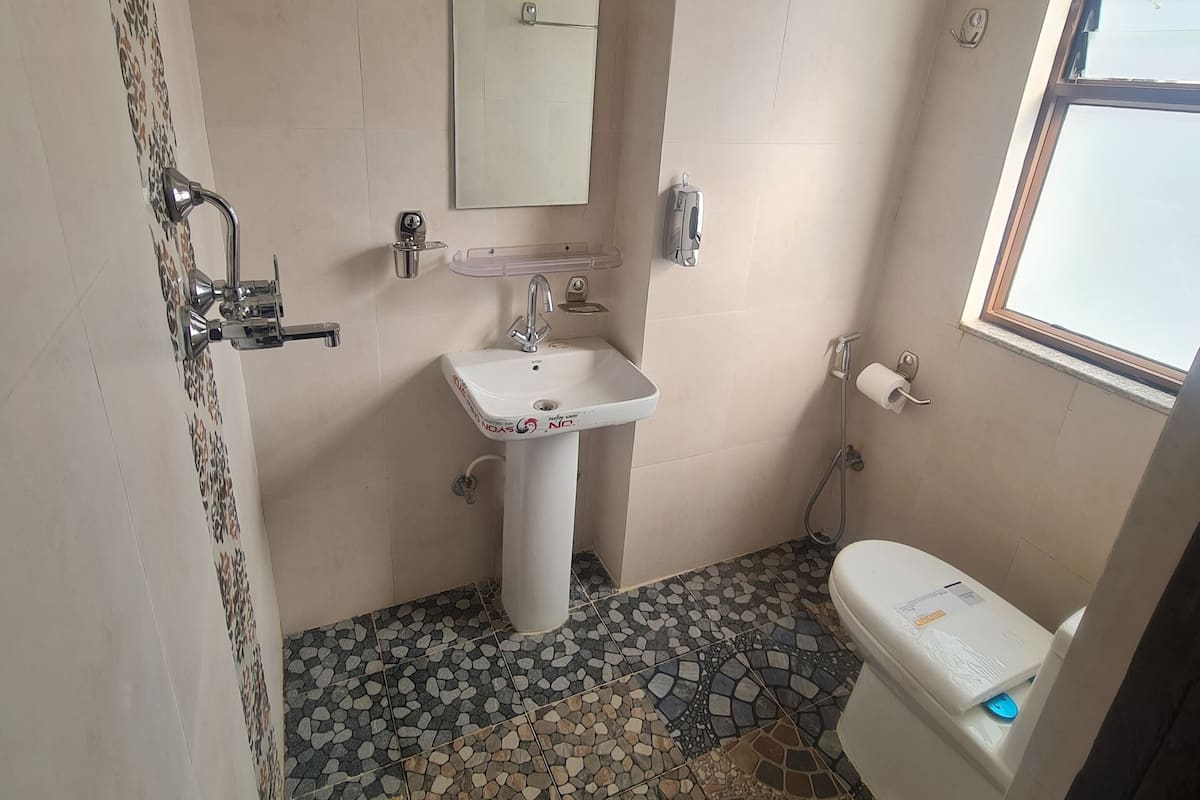 A bathroom with a white sink, a mirror, a toilet, and a shower. The floor has a mosaic tile pattern.