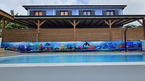 Una piscina con un murale subacqueo, un pontile in legno e una casa sullo sfondo.