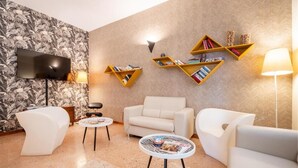 Una sala de estar moderna con una televisión de pantalla plana, dos sofás blancos, una mesa de centro y un papel tapiz estampado.