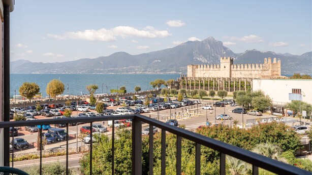 Vista costera con un estacionamiento, un edificio parecido a un castillo y montañas al fondo.