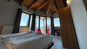 Un dormitorio con techo de madera, una cama, un ventanal y un balcón con sillas rojas.