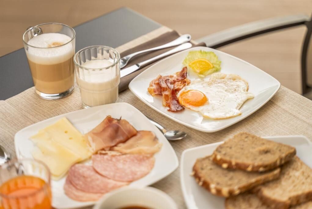A breakfast setting with plates of eggs, bacon, cheese, and toast, accompanied by two glasses of milk and a cup of coffee.