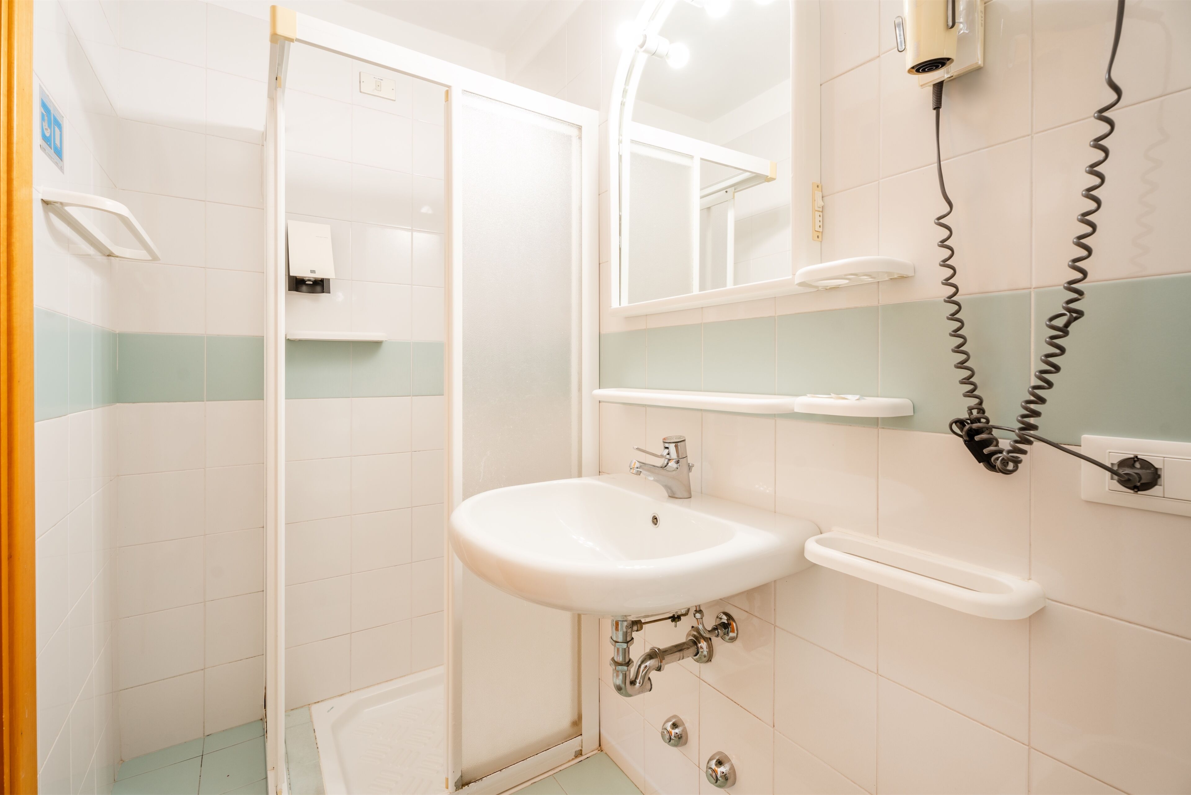 Een badkamer met een witte wastafel, een spiegel, een handdroger en een douche.