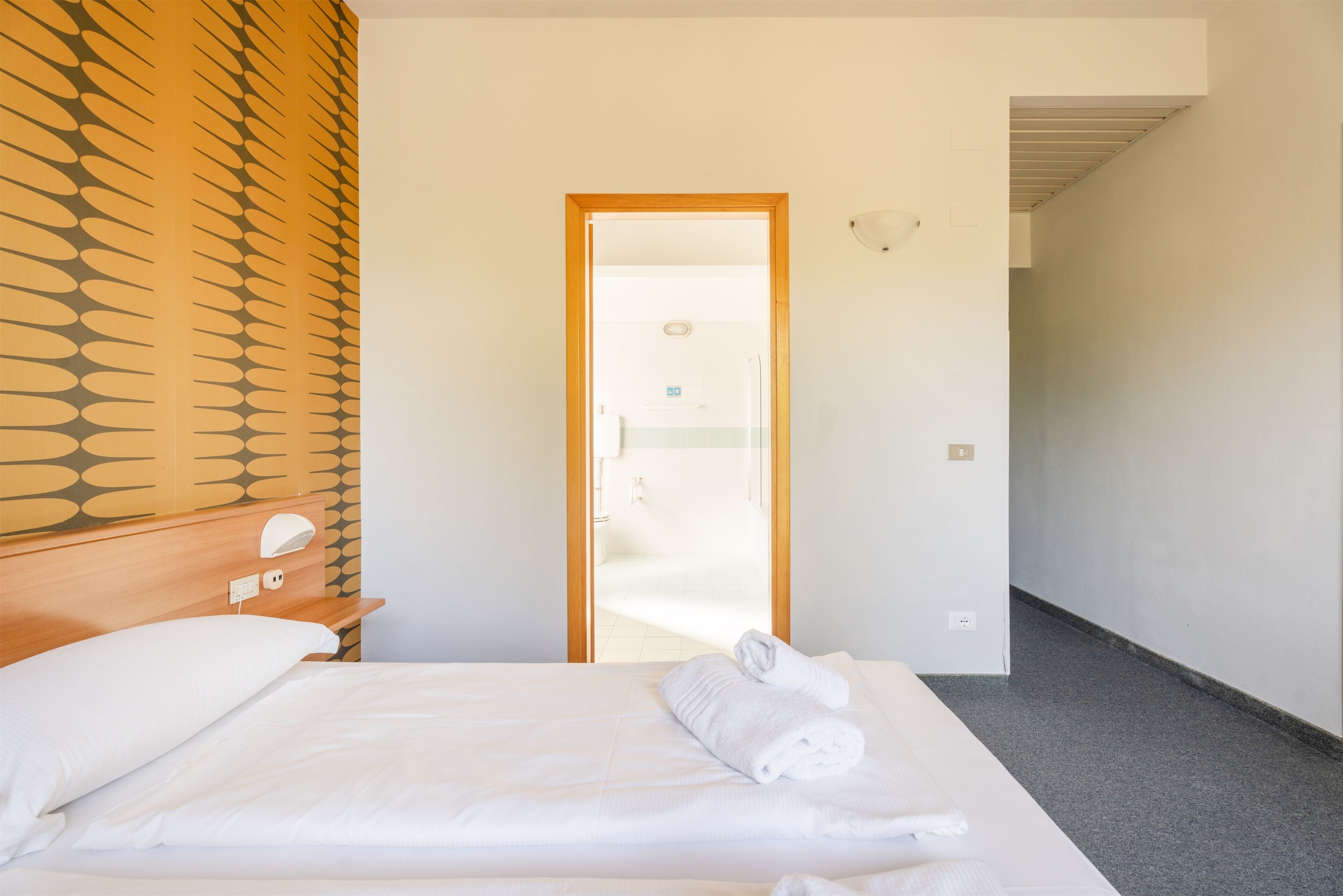 A hotel room with a bed, a wooden headboard, a mirror, and a view of the bathroom through an open door.