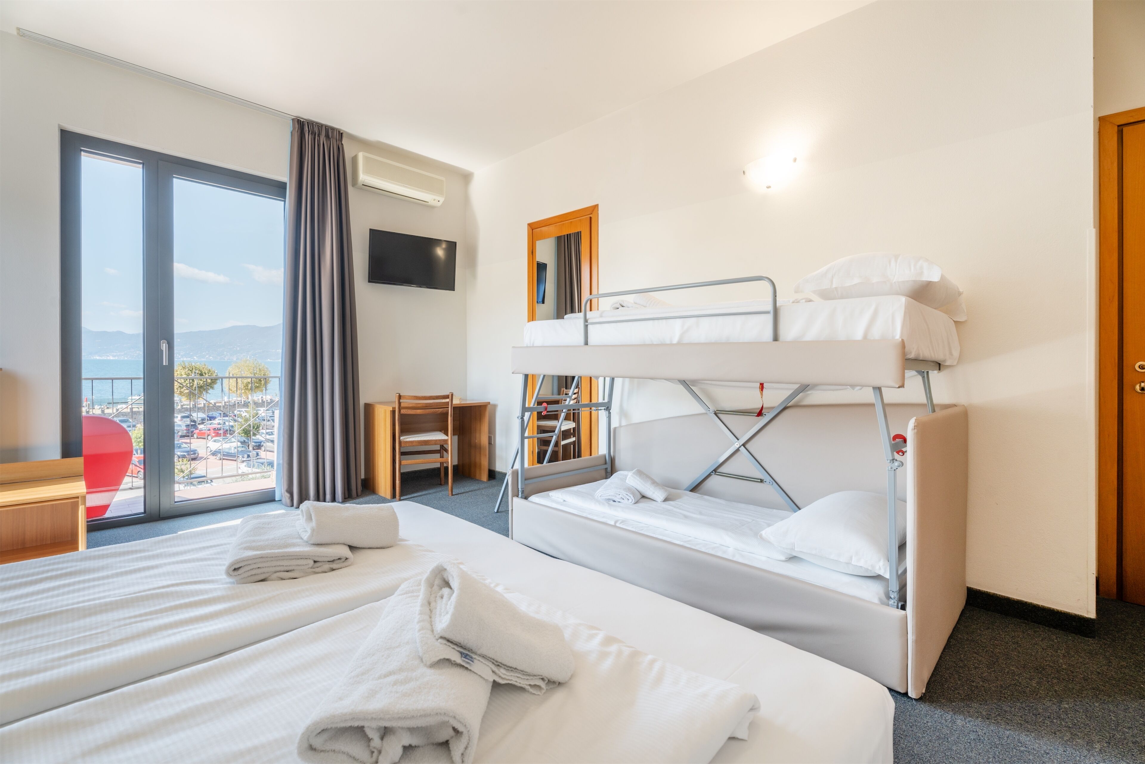 A hotel room with a large bed, a bunk bed, a desk, a chair, and a TV on the wall.
