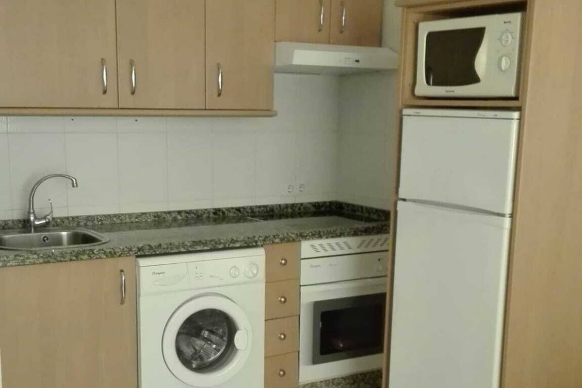 A compact kitchen with wooden cabinets, a built-in washing machine, a microwave, and a stove.