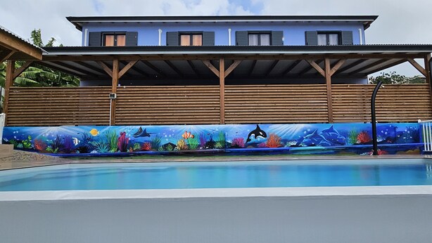 A swimming pool with an underwater mural, a wooden deck, and a house in the background.