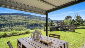 An outdoor seating area with a table, chairs, and a view of a mountainous landscape. - Molla Eco Lodge Kangaroo Valley (Wattamolla)
