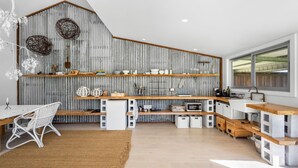 A modern kitchen with wooden shelves, a white dining area, and a large window. - Molla Eco Lodge Kangaroo Valley (Wattamolla)