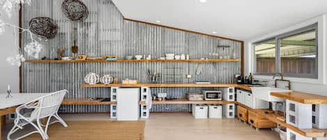 A modern kitchen with wooden shelves, a white dining area, and a large window.