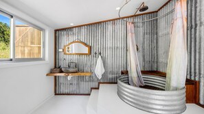 Ein Badezimmer im rustikalen Stil mit einem großen Waschbecken, einem Spiegel und einer Dusche mit Duschvorhang.