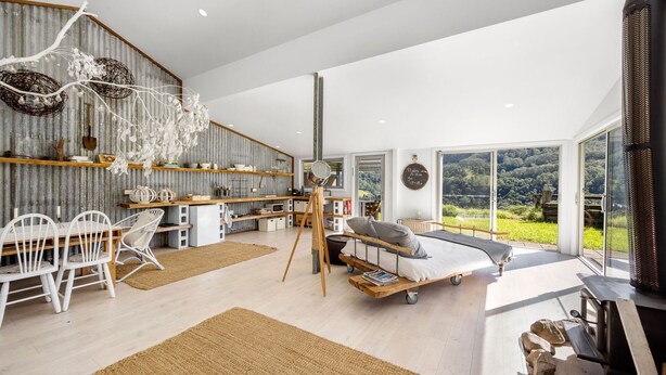 A spacious living area with a large window offering a view of the outdoors, a cozy seating area with a bed, and a kitchen with wooden shelves. - Molla Eco Lodge Kangaroo Valley (Wattamolla)