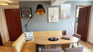Ein gemütlicher Essbereich mit einem runden Tisch, einer gepolsterten Bank und Stühlen, einer schwarzen Stehlampe und gerahmten Kunstwerken an der Wand.