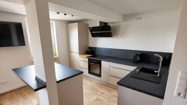 Eine moderne Küche mit schwarzem Arbeitsplatz, weißen Schränken, einem eingebauten Backofen und einer schwarzen Dunstabzugshaube.