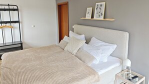 Ein Schlafzimmer mit Bett, Nachttisch, Lampe und Wandregal mit Bildern.