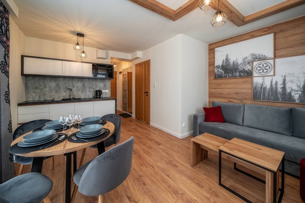 Uma sala de estar moderna com área de jantar, um sofá cinzento e uma mesa de centro de madeira.