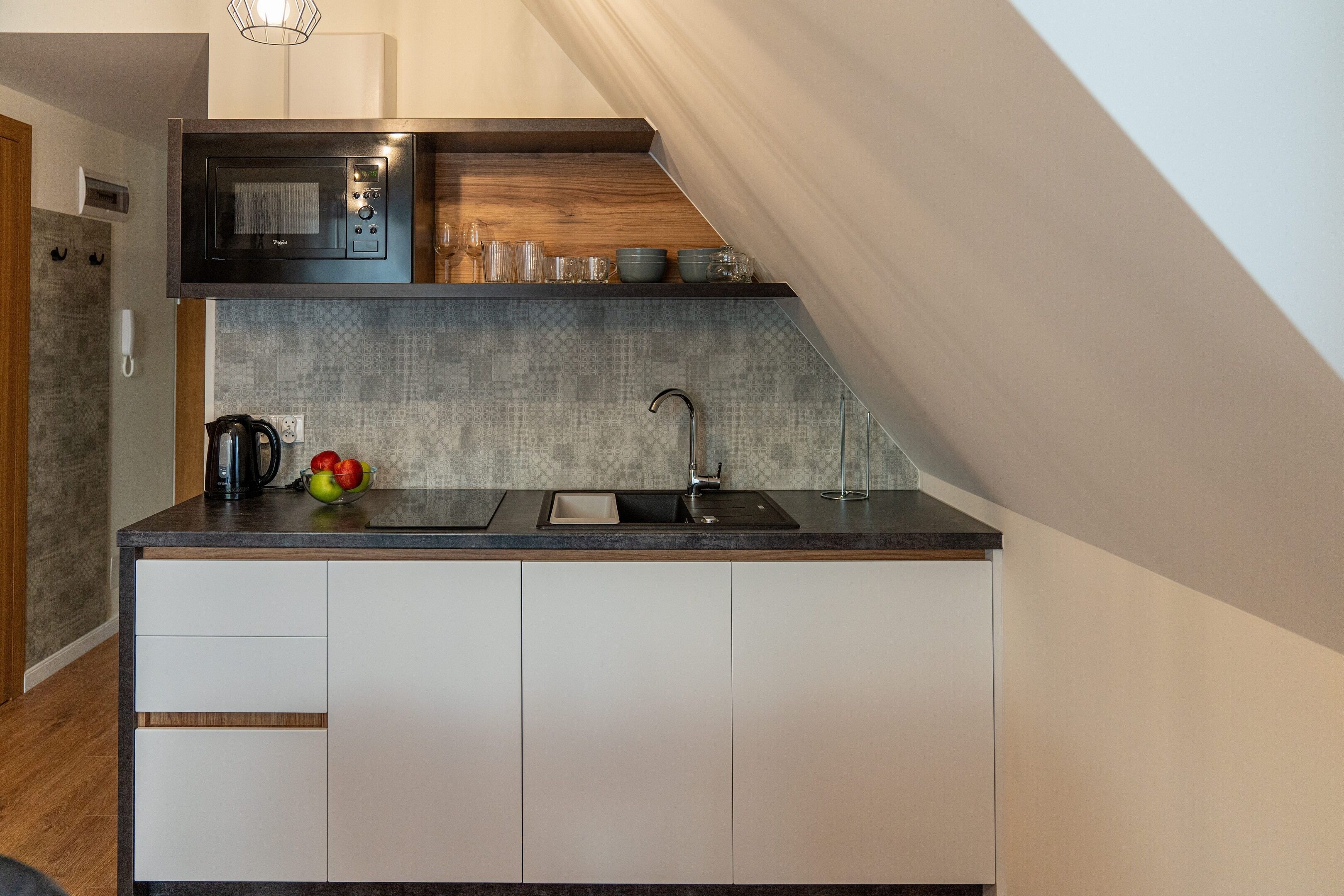 A compact kitchen with a microwave, sink, and a wooden shelf above the countertop.
