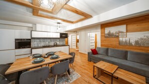 A modern kitchen with white cabinets, a built-in oven, and a dining area with a wooden table and grey chairs. - Sun & Snow Resorts F Białka Tatrzańska (Bukowina Tatrzanska)
