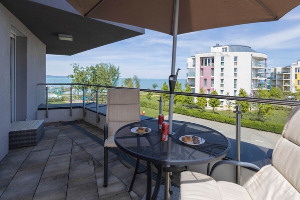A balcony with a table, chairs, and a view of the sea and buildings.