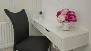 Un escritorio blanco con un florero, una silla y un radiador al fondo.