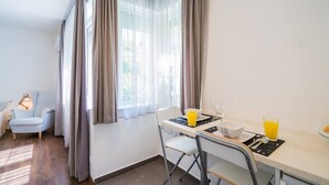 A small, bright room with a dining table, chairs, and a window with curtains. - LB - Phoenix Apartman Siófok (Siófok)