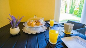 A breakfast setup with croissants, orange juice, and a coffee cup on a table with a yellow wall and a view of greenery outside. - LB - Phoenix Apartman Siófok (Siófok)