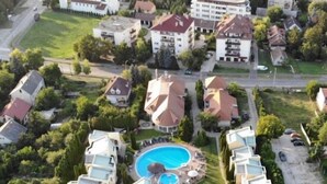Oversigtsbillede af et boligområde med moderne lejlighedskomplekser, en central swimmingpool og grøn bevoksning omkring.