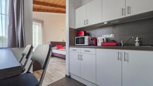 Et moderne køkken med hvide skabe, en mikroovn og en rød elkedel. Der er et spiseområde med et bord og stole.