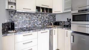 Una cocina moderna con armarios blancos, salpicadero de azulejos, electrodomésticos de acero inoxidable y una cafetera en la encimera.