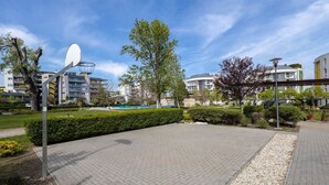 Un espacio al aire libre pavimentado, con una antena parabólica, árboles y edificios residenciales al fondo.