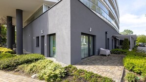 Un edificio moderno con fachada de vidrio curva, techo plano y un patio pavimentado con una silla blanca.