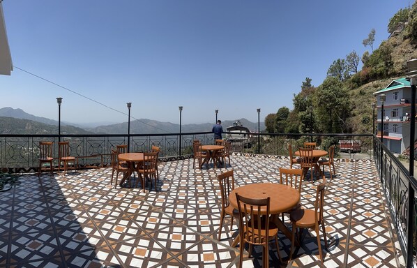 A terrace with a patterned floor, outdoor seating, and a view of distant mountains.