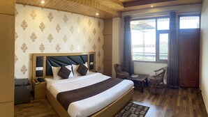 A hotel room with a large bed, a desk, two chairs, a small table, a telephone, and a nightstand.