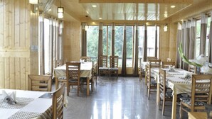 A wooden interior with multiple dining tables and chairs, large windows, and ceiling lights.