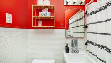 Une salle de bain avec un mur rouge, un sol carrelé de blanc, des toilettes blanches, un lavabo avec un miroir et un rideau de douche à motifs noirs.