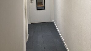A narrow hallway with a white door at the end, a small mirror on the door, and dark grey tiled flooring. - La Campagne Proche de Paris - Chez Marie-louise (Montreuil)