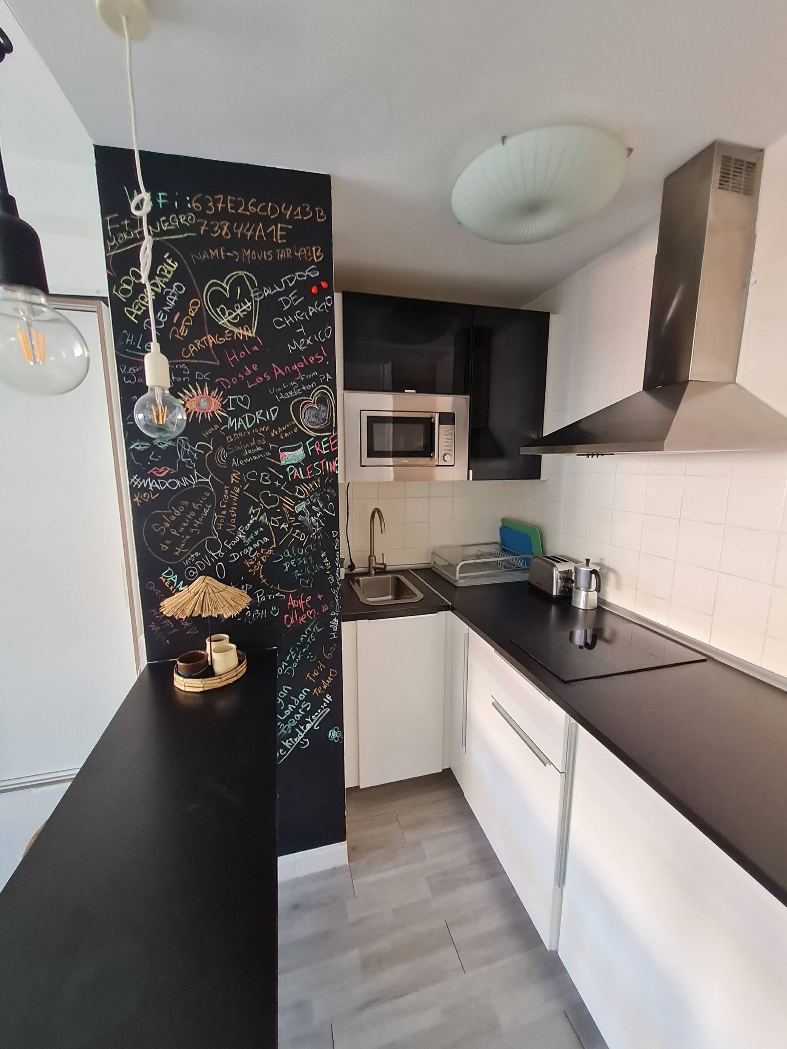 Une cuisine compacte avec un tableau noir couvert de divers écrits et dessins, un four à micro-ondes, un évier et une hotte de cuisine en acier inoxydable.