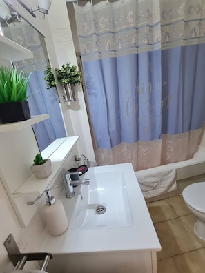 A bathroom with a white sink, a mirror, a shower curtain with a pattern, and a toilet.