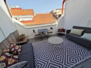 A small outdoor patio with a round table, two chairs, a sofa, and a patterned rug.